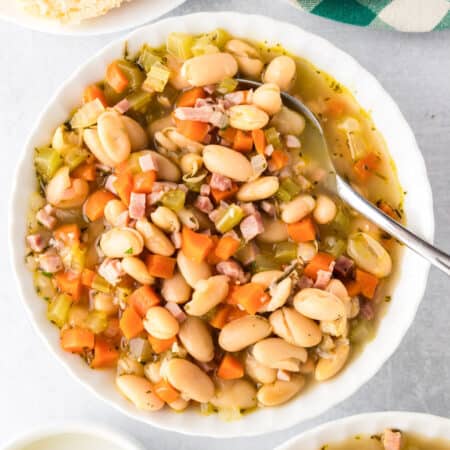 A bowl of white bean and ham soup with diced ham, carrots, celery, and rich broth, served with a spoon in the bowl.