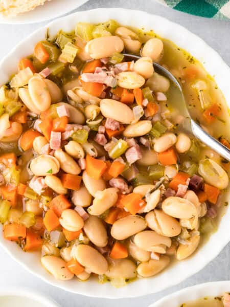 A bowl of white bean and ham soup with diced ham, carrots, celery, and rich broth, served with a spoon in the bowl.