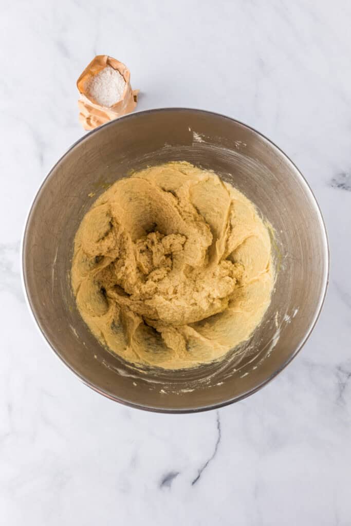 A metal mixing bowl with creamed butter and sugar with a pouch of instant vanilla pudding nearby for Oreo pudding cookies.