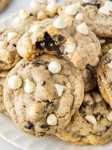 A plate of Oreo pudding cookies with white chocolate chips on top; one cookie has a bite taken out of it.