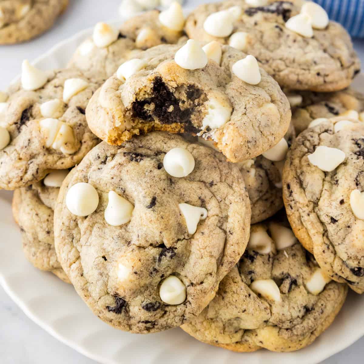A plate of Oreo pudding cookies with white chocolate chips on top; one cookie has a bite taken out of it.