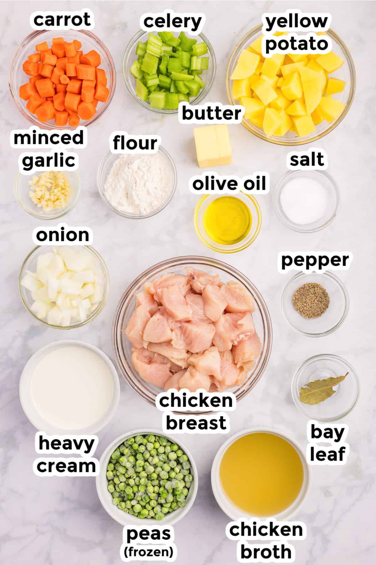 Top-down view of labeled bowls with ingredients for creamy chicken stew, including chicken breast, vegetables, seasonings, flour, butter, olive oil, heavy cream, and chicken broth.