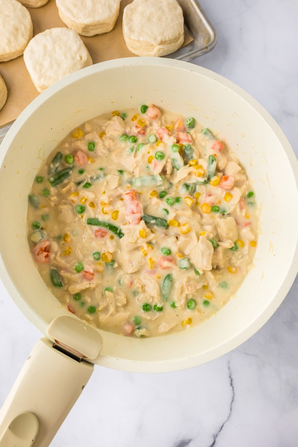 A white skillet filled with creamy chicken and mixed vegetables, the filling for Biscuit Chicken Pot Pie.