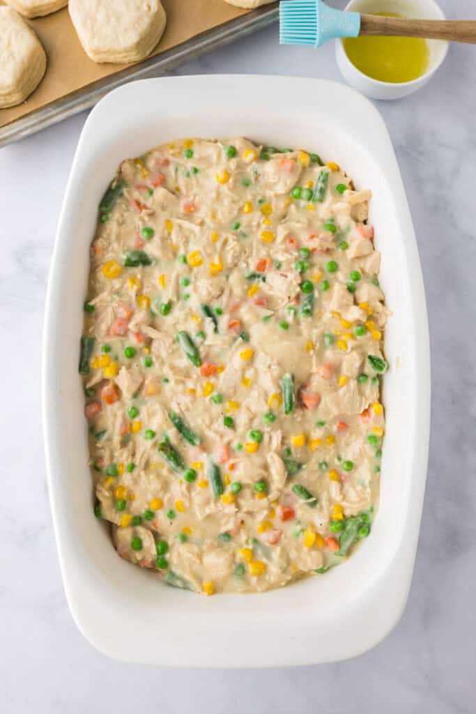 A white baking dish filled with creamy Biscuit Chicken Pot Pie packed with chicken, peas, carrots, corn, and green beans.