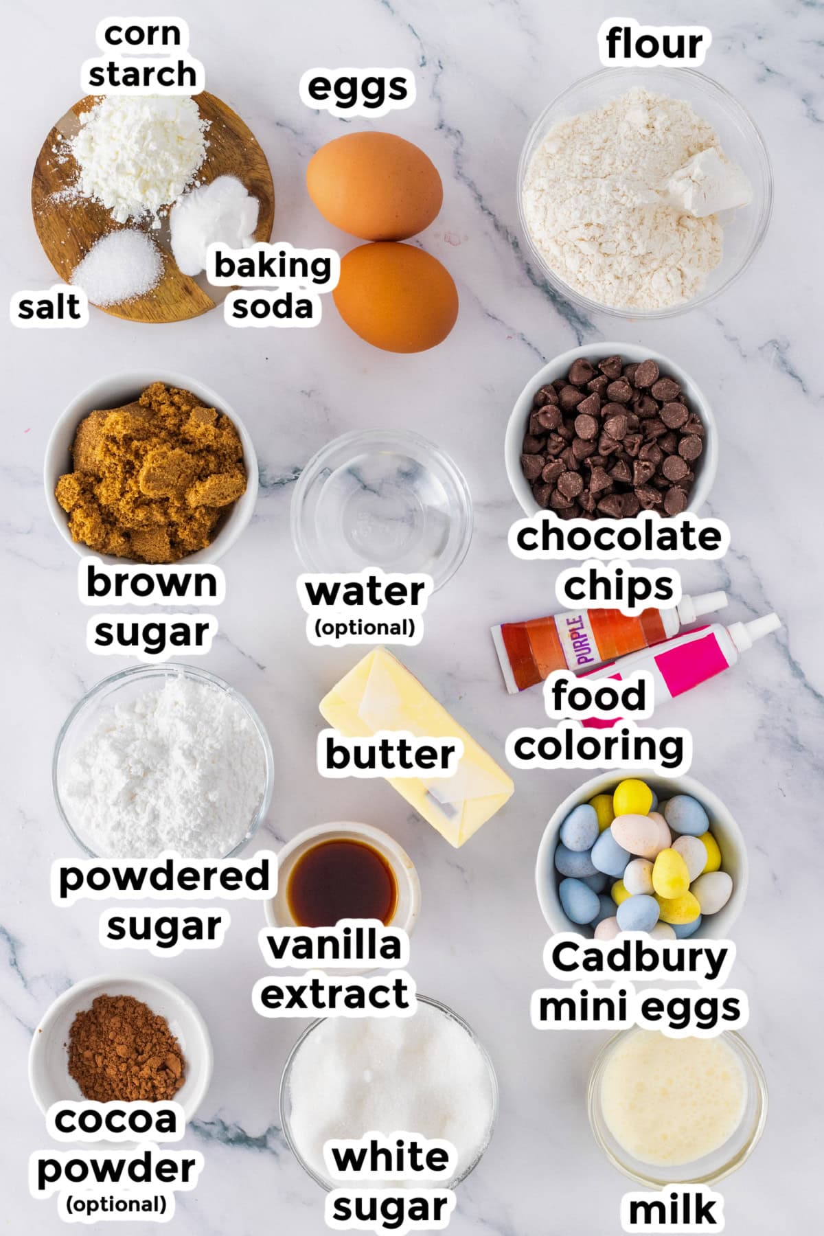 Various baking ingredients are arranged on a white surface, each labeled, including flour, eggs, sugars, butter, chocolate chips, milk, food coloring, and elements perfect for making cadbury mini egg cookie bars.