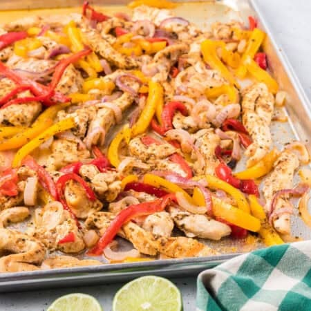 Sheet pan Chicken Fajitas with cooked chicken strips, red and yellow bell peppers, and onions, served alongside a bowl of salsa and lime halves for a fresh burst of flavor.