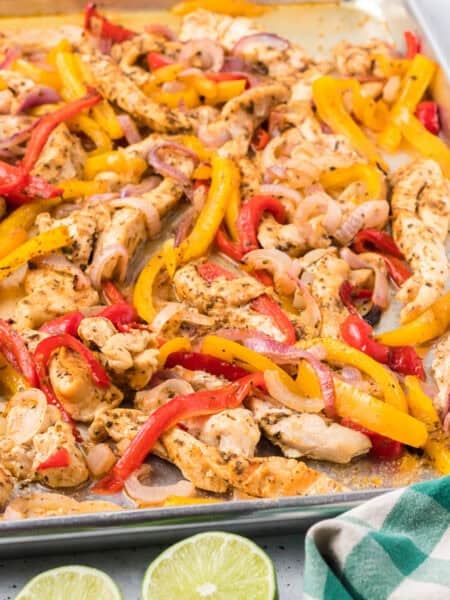Sheet pan Chicken Fajitas with cooked chicken strips, red and yellow bell peppers, and onions, served alongside a bowl of salsa and lime halves for a fresh burst of flavor.