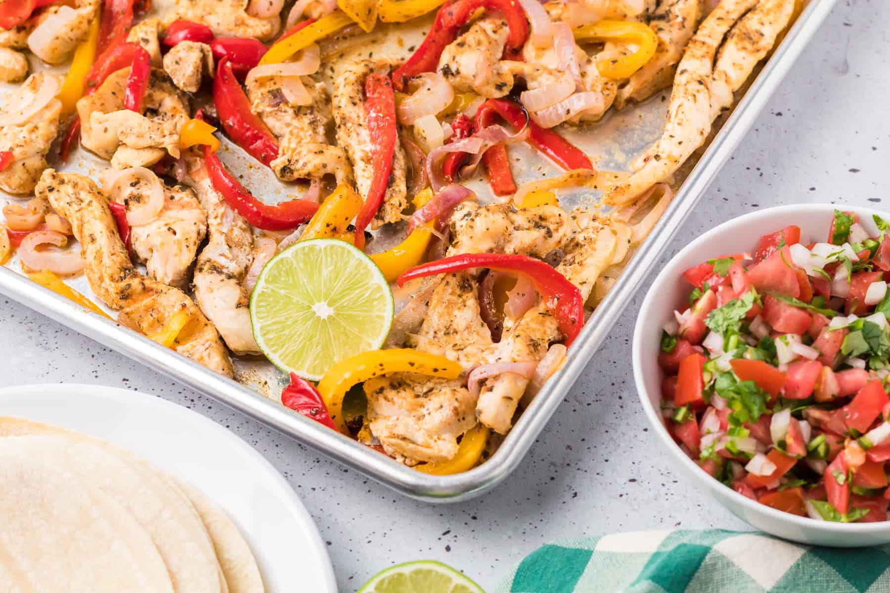 Sheet pan Chicken Fajitas with tender chicken strips, colorful bell peppers, onions, and lime, served alongside warm tortillas and a bowl of fresh pico de gallo.