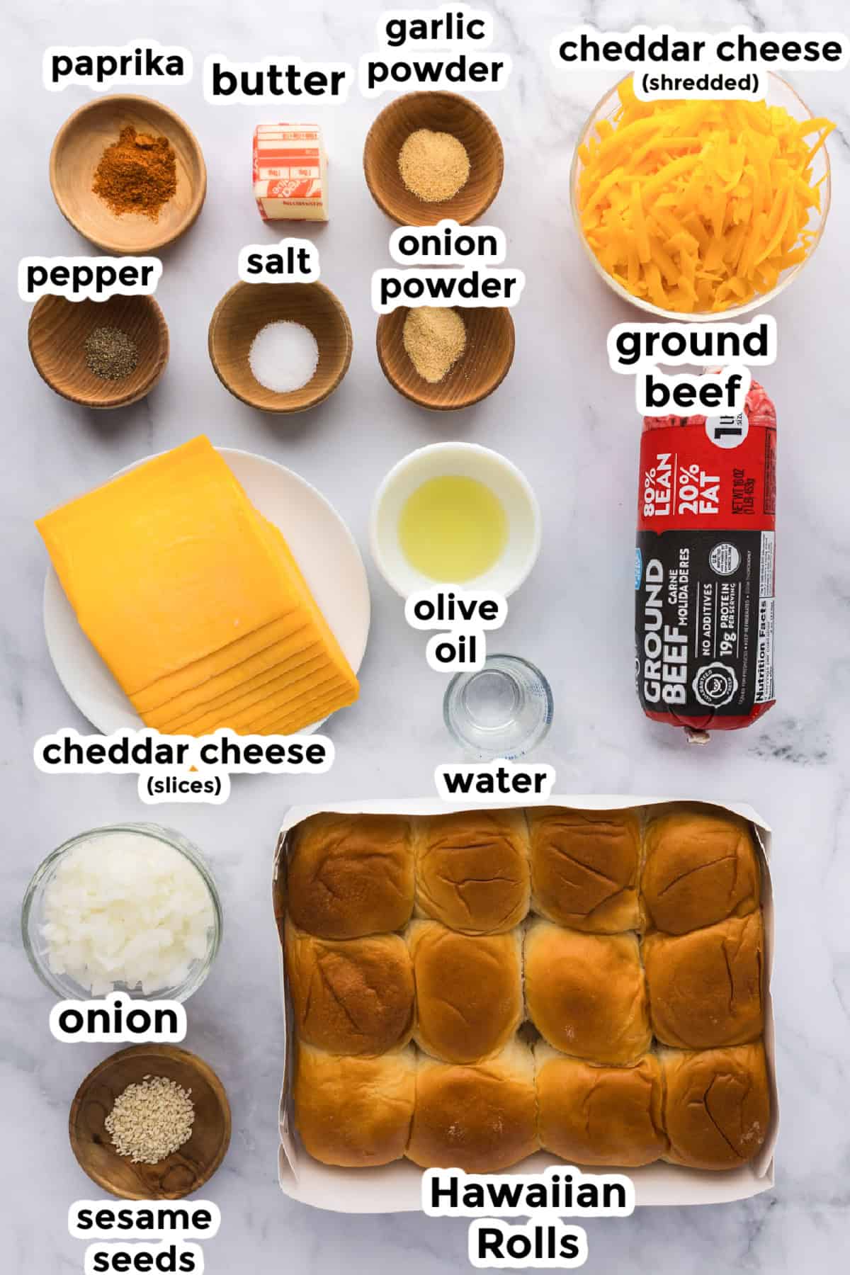 Ingredients for cheeseburger sliders are arranged on a table, featuring ground beef, Hawaiian rolls, shredded and sliced cheddar cheese, buttery sesame seeds, seasonings, olive oil, and savory onions.