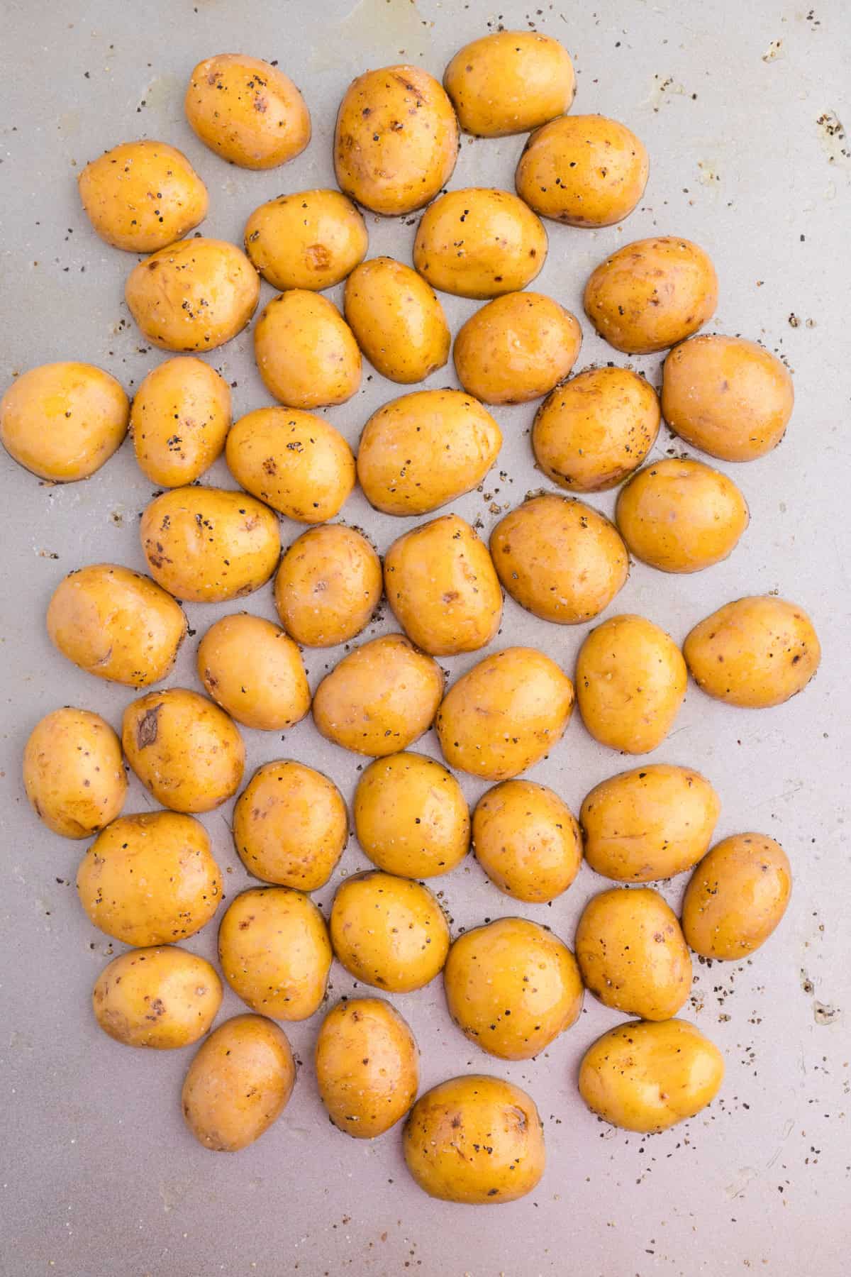 Small golden potatoes seasoned with black pepper and salt, spread out on a baking sheet to bake to be added to a burger bowl.
