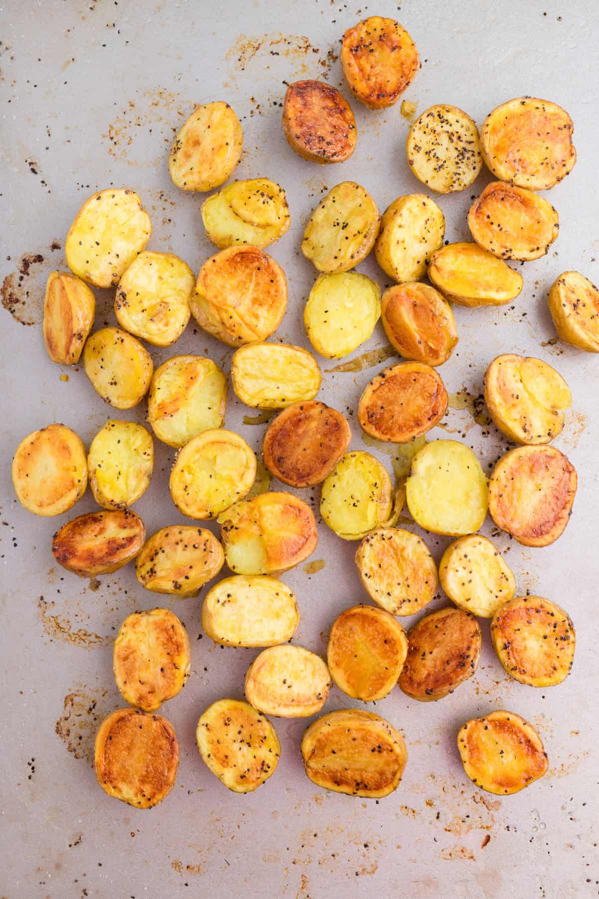 Halved, roasted baby potatoes with seasoning scattered on a baking sheet for adding to a burger bowl.