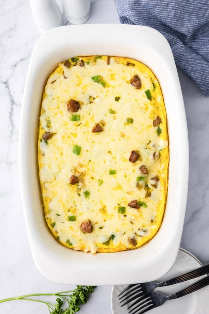 A chicken sausage egg bake breakfast casserole with visible pieces of sausage, green bell pepper, and cheese in a white rectangular dish on a marble countertop.