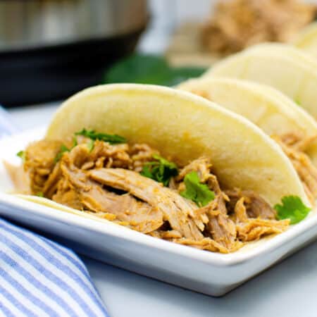 A close-up of instant pot carnitas tacos with cilantro on soft corn tortillas, served on a white rectangular plate.