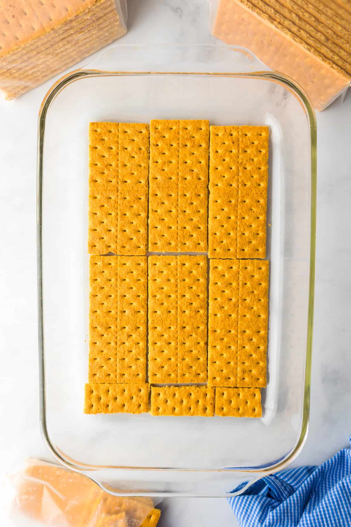 A layer of graham crackers arranged neatly in a glass baking dish, ready to become the base for a delicious lemon eclair icebox cake.