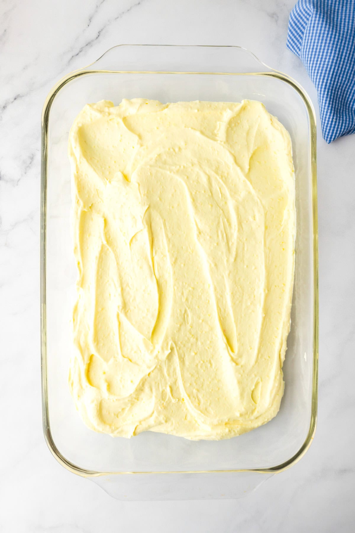 Glass baking dish filled with evenly spread cheesecake pudding filling for a lemon eclair icebox cake.