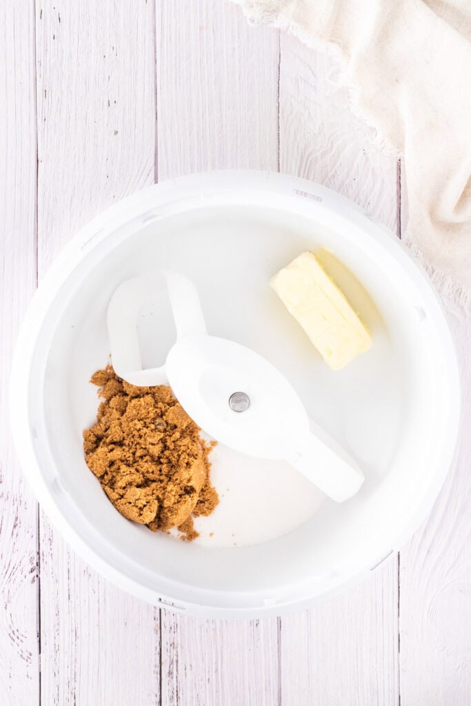 A mixing bowl with brown sugar, white sugar, and a stick of butter on a white wooden surface—ready to start baking mini egg chocolate chip cookies.