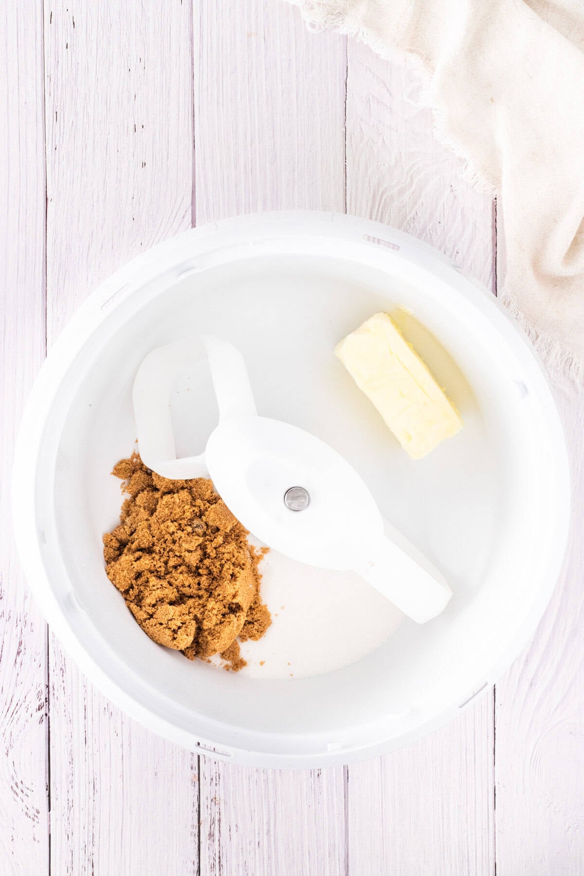 A mixing bowl with brown sugar, white sugar, and a stick of butter on a white wooden surface—ready to start baking mini egg chocolate chip cookies.