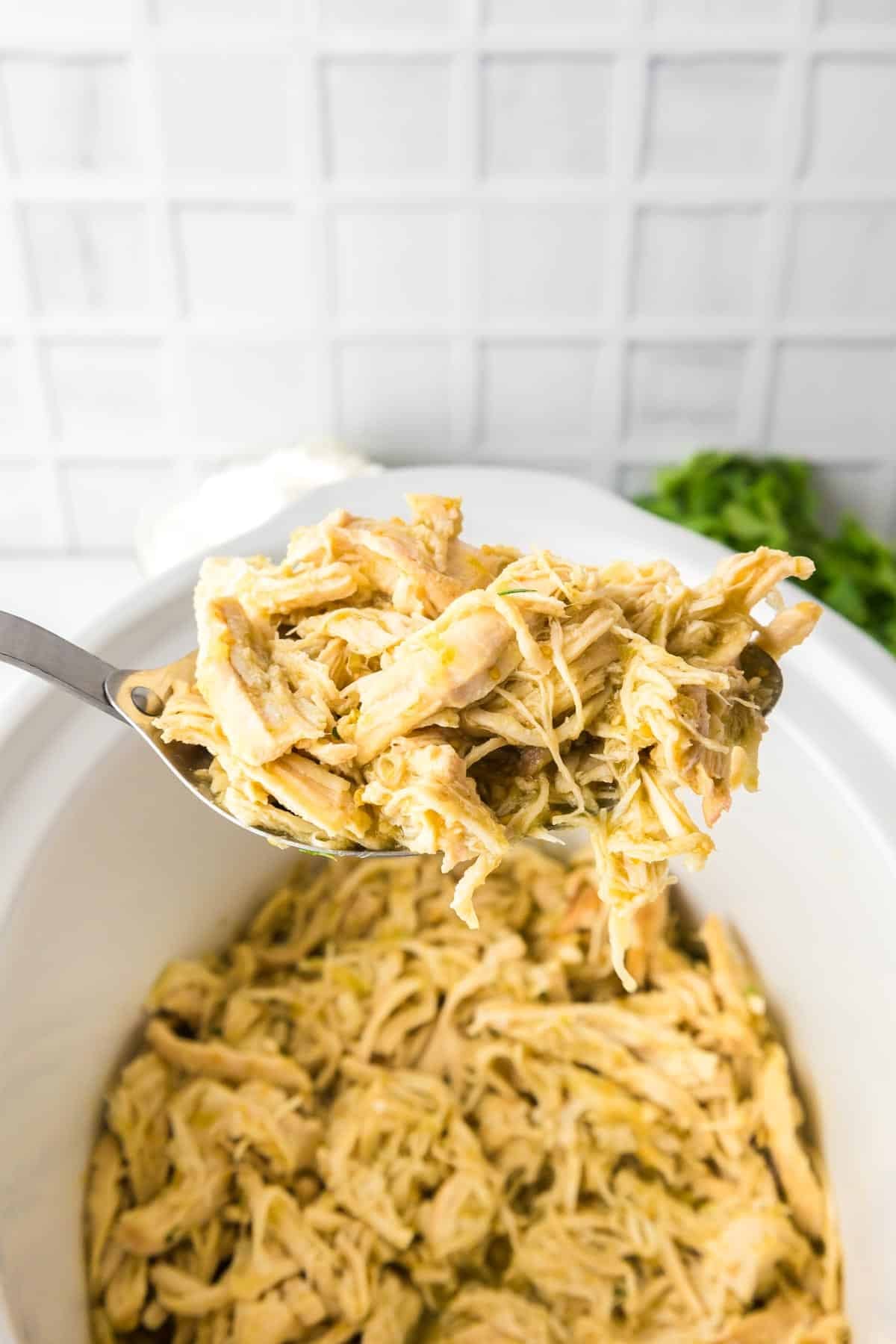 A spoonful of Slow Cooker Salsa Verde Chicken over a slow cooker full of tender, shredded chicken.