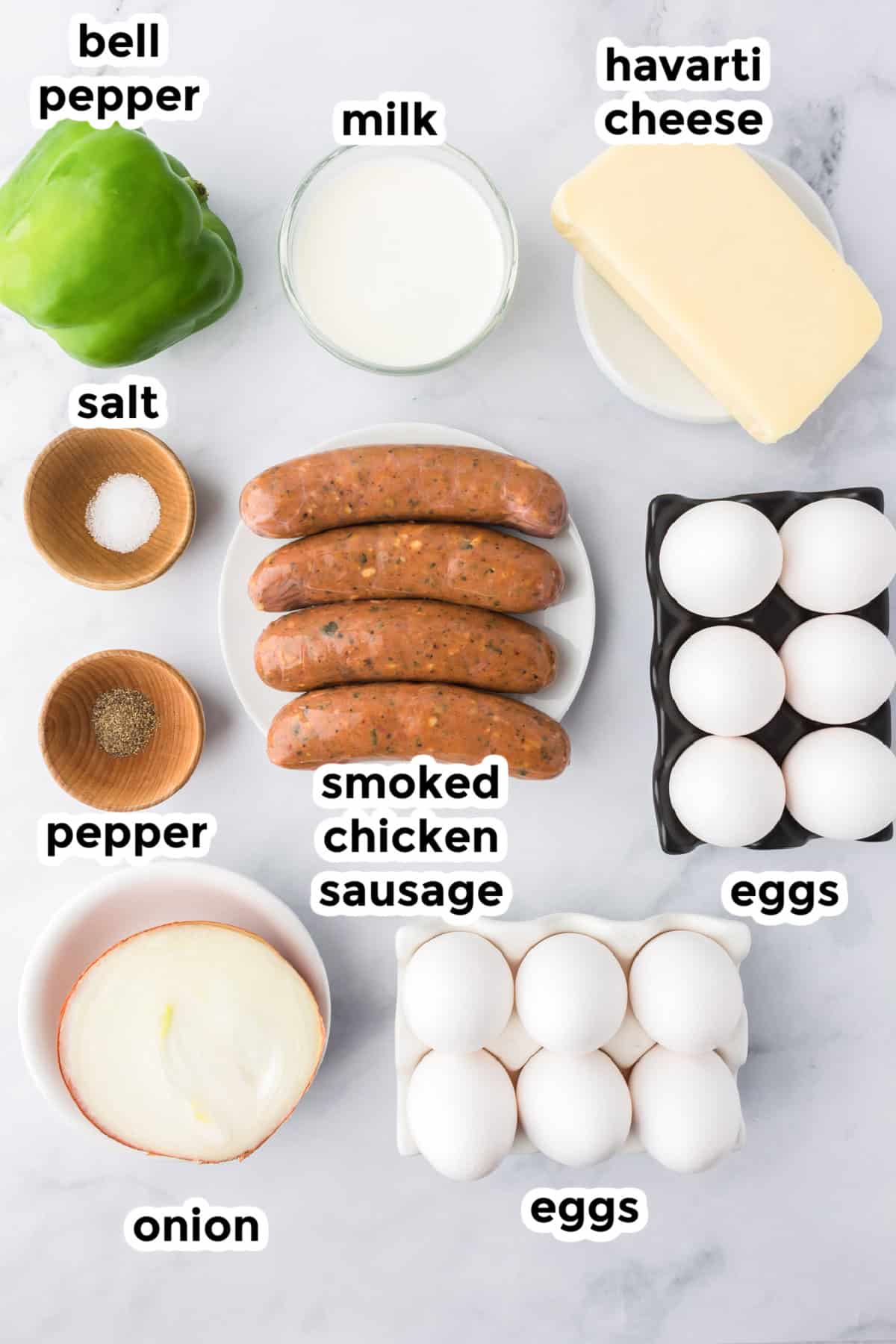 Top-down view of ingredients for a chicken sausage egg bake on a white surface, including bell pepper, milk, Havarti cheese, salt, pepper, smoked chicken sausage, eggs, and onion&mdash;perfect for a breakfast casserole. Each item is clearly labeled.