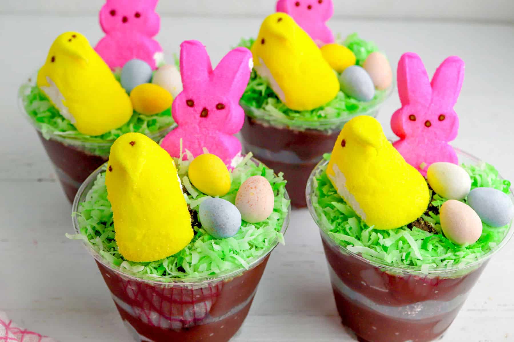 Clear plastic cups filled with layered chocolate pudding, topped with green shredded coconut, colorful candy eggs, and marshmallow bunny and chick shapes make festive Easter dirt cups.