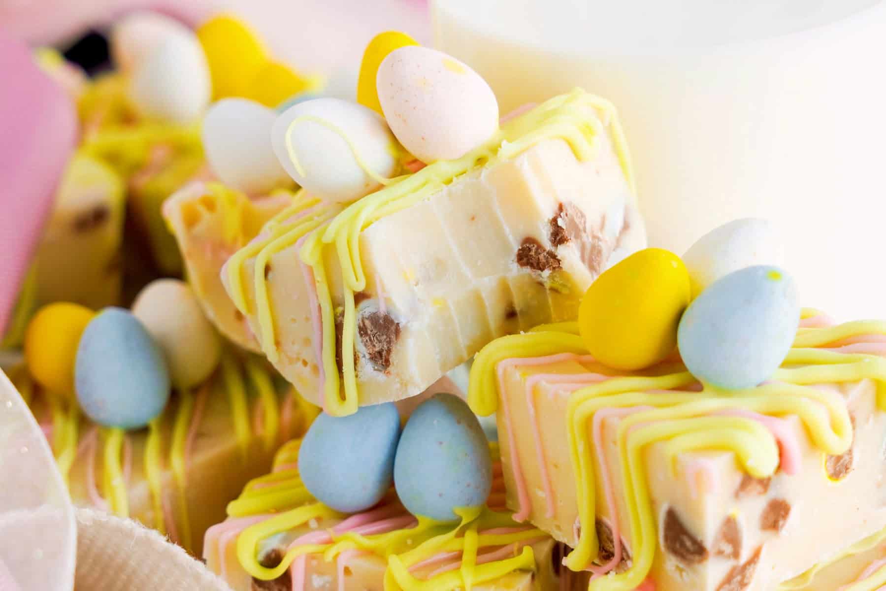 Close-up of Easter mini egg fudge pieces, topped with pastel-colored candy eggs and drizzled with yellow and pink icing.