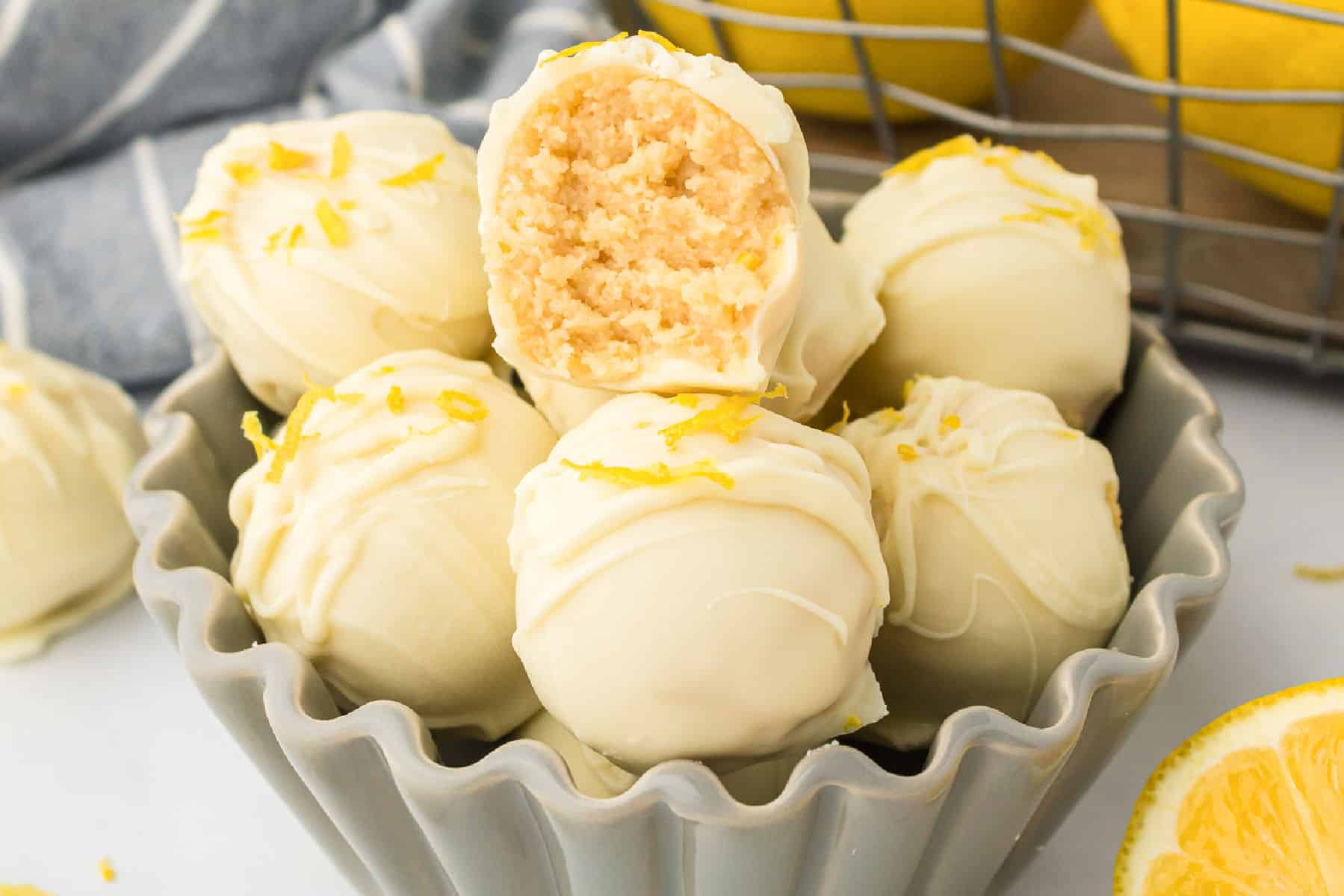 A bowl filled with white chocolate-covered lemon truffle Oreo balls, one with a bite taken out, garnished with fresh lemon zest.