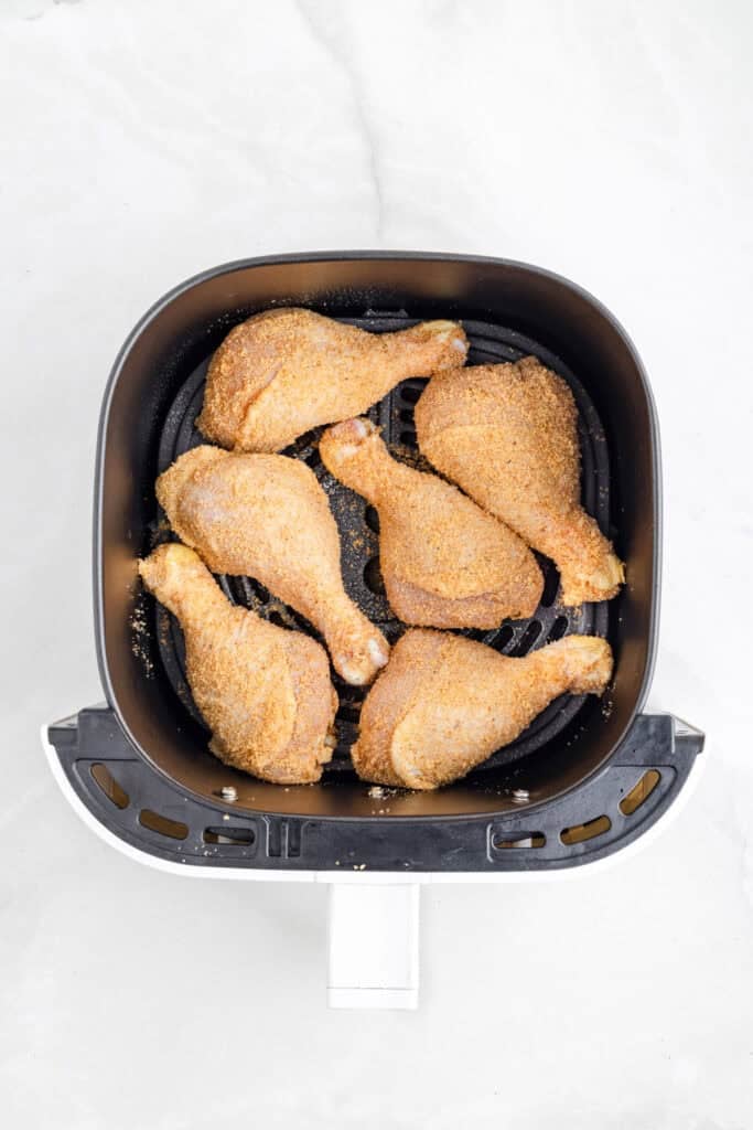 Six shake and bake air fryer chicken drumsticks arranged in a single layer inside an air fryer basket on a light surface.