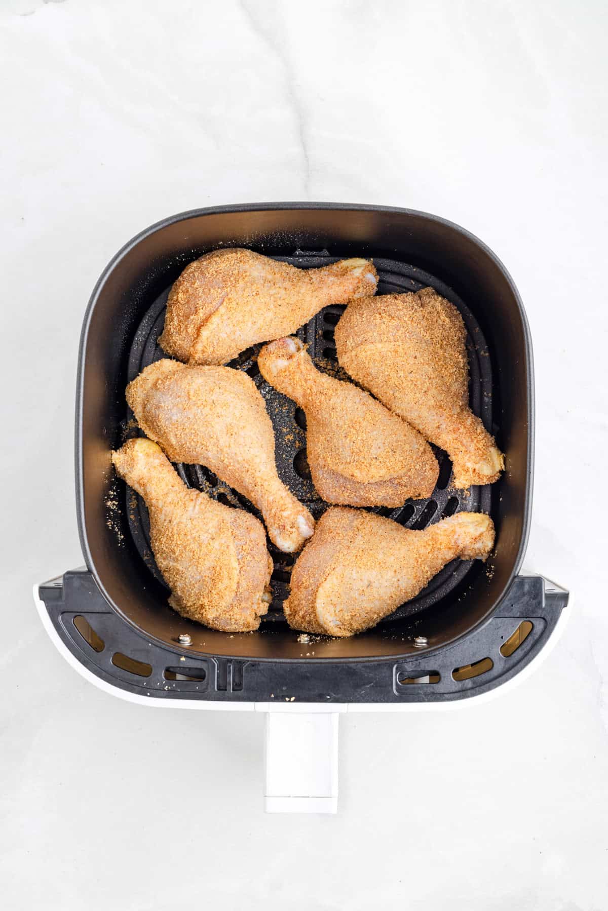 Six shake and bake air fryer chicken drumsticks arranged in a single layer inside an air fryer basket on a light surface.