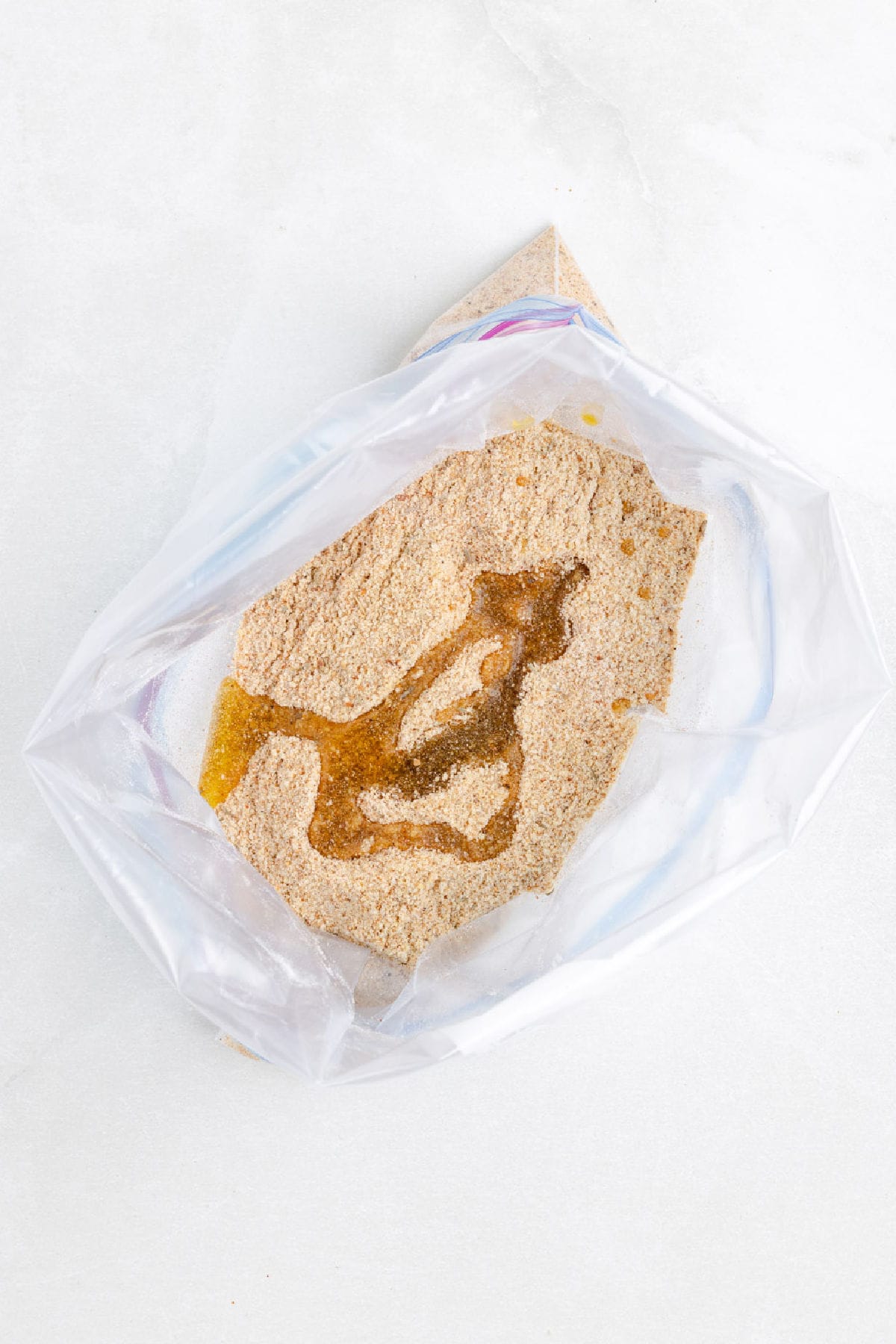 A clear plastic bag partially filled with bread crumbs and a small amount of oil, perfect for prepping shake and bake air fryer chicken drumsticks.