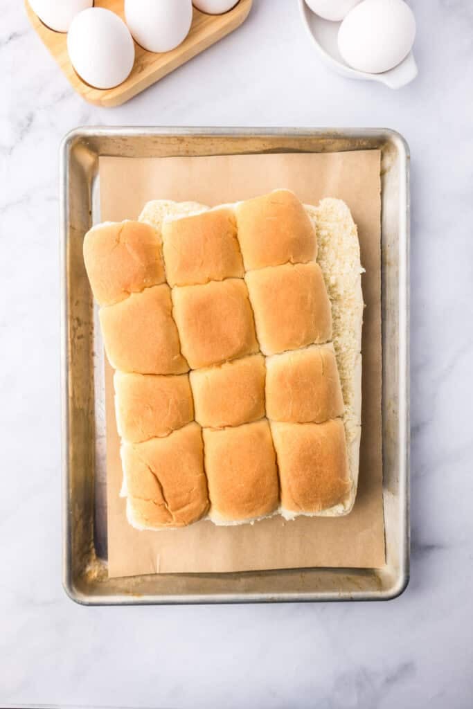 A sheet pan with a block of connected slider buns on parchment paper, perfect for making breakfast sliders.