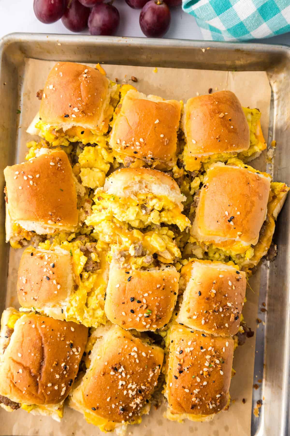 A baking sheet with sliders made of golden brown buns filled with scrambled eggs, sausage and cheese.
