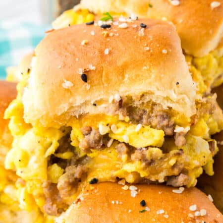 Single vreakfast slider with scrambled eggs, sausage, and cheese inside soft, golden buns sprinkled with seasoning.