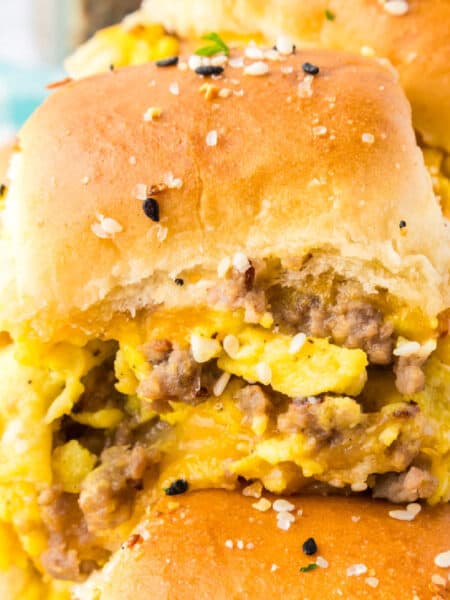 Single vreakfast slider with scrambled eggs, sausage, and cheese inside soft, golden buns sprinkled with seasoning.