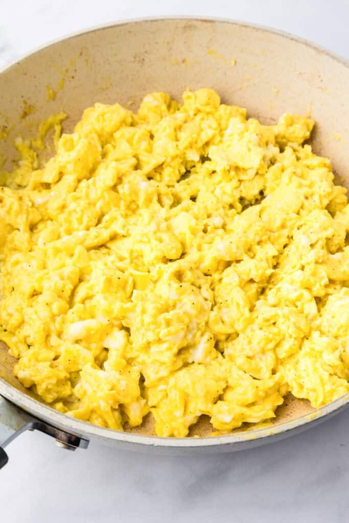 Scrambled eggs cooking in a nonstick skillet on a light-colored surface, perfect for making breakfast sliders.