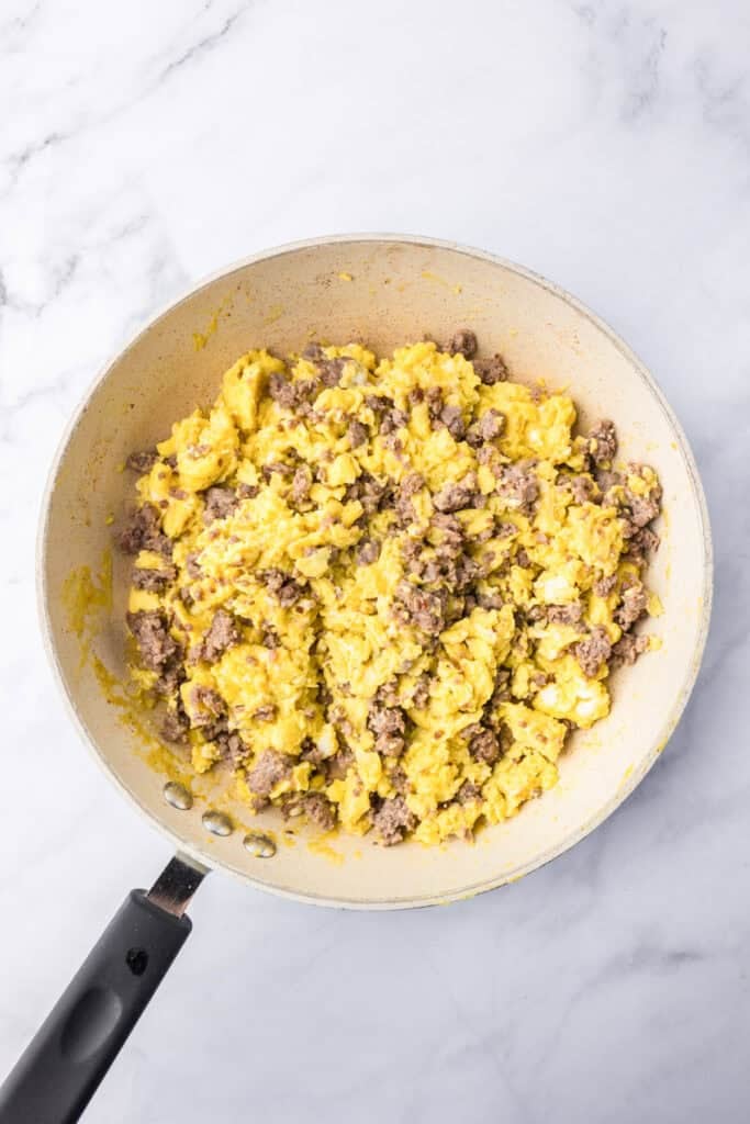 A frying pan filled with scrambled eggs mixed with cooked ground sausage, perfect for making delicious breakfast sliders, set on a marble countertop.