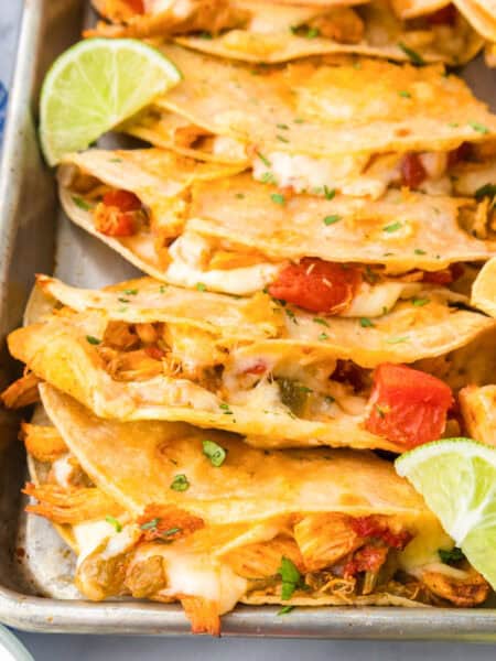 A baking tray filled with four crispy baked chicken tacos topped with lime, tomato and cilantro.