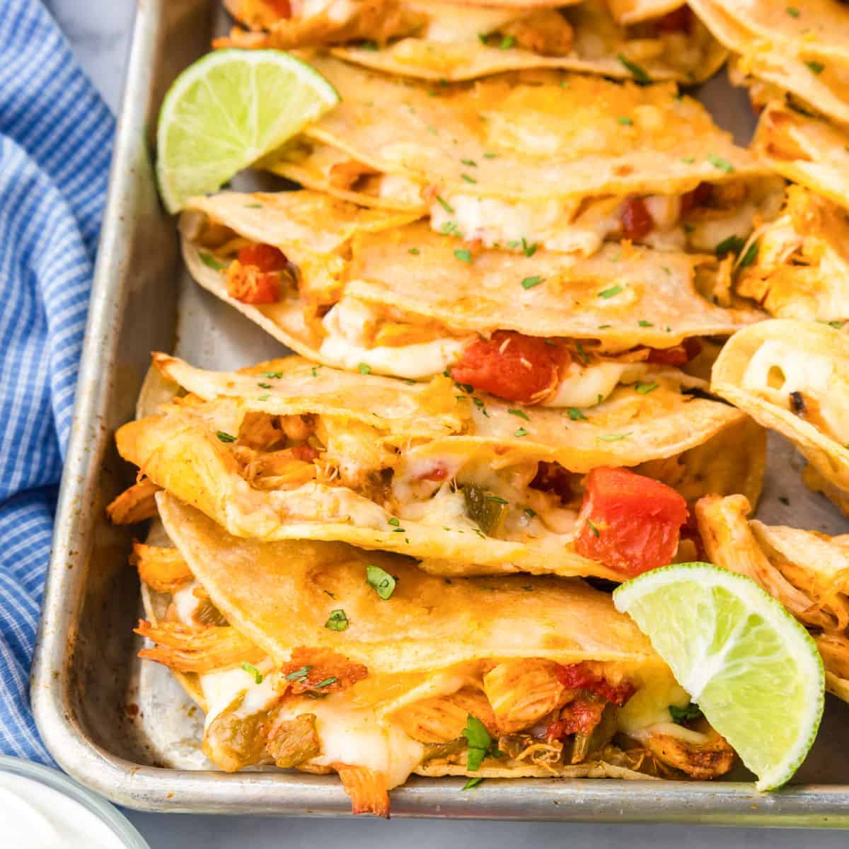 A baking tray filled with four crispy baked chicken tacos topped with lime, tomato and cilantro.