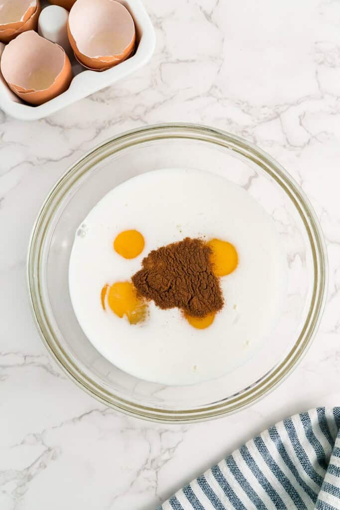 A glass bowl containing milk, eggs, and cinnamon sits on a counter for french bread french toast.