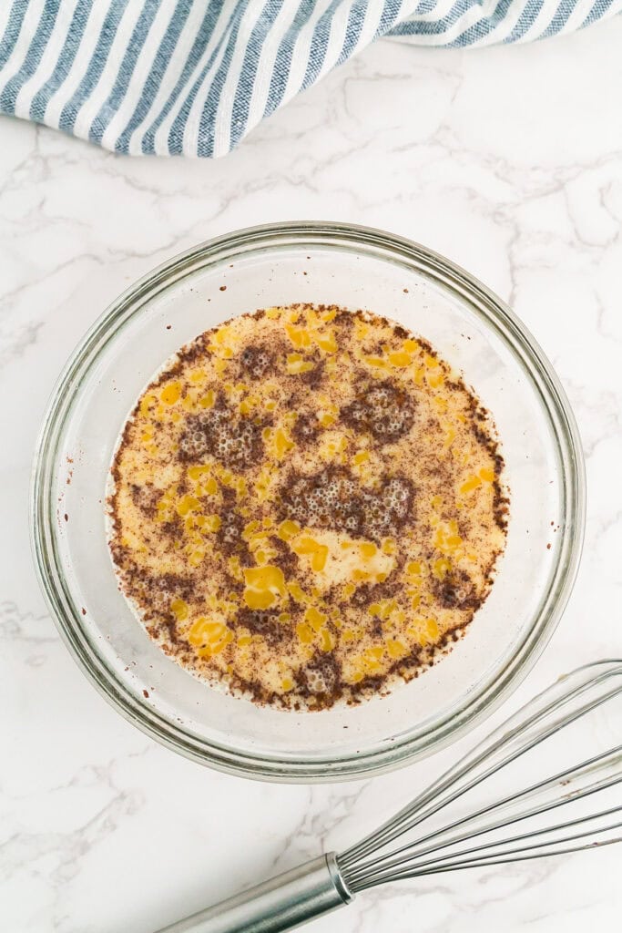 A glass bowl containing a cinnamon egg custard mixture for french bread french toast.