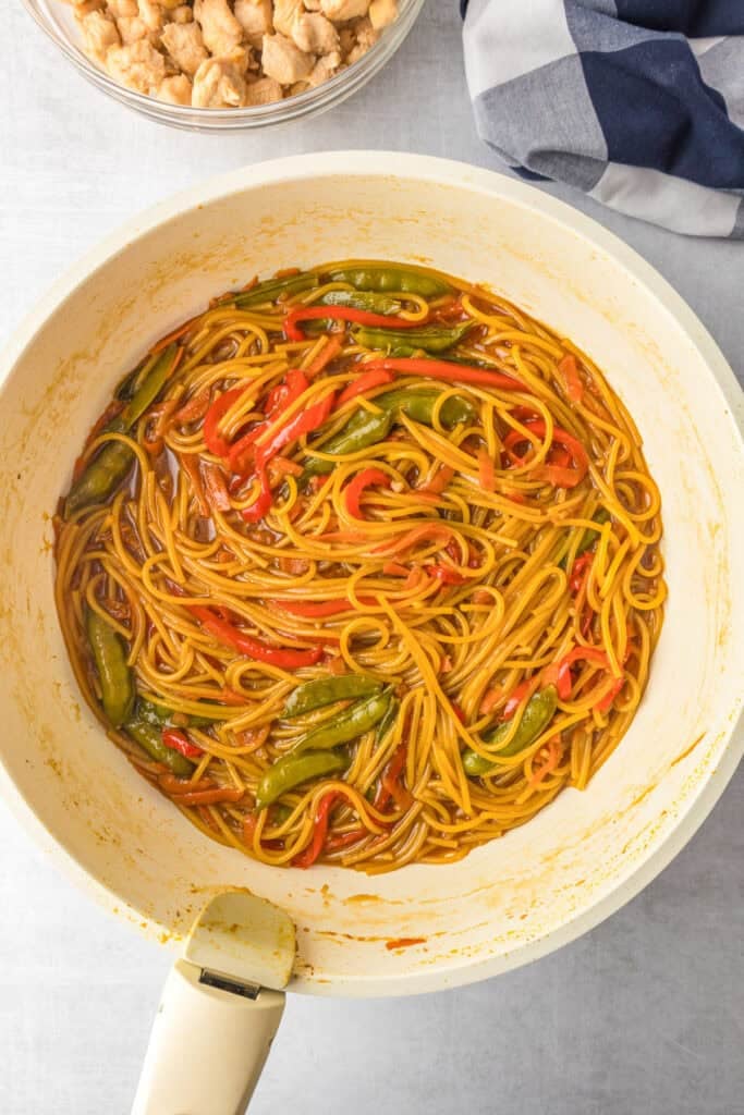 A pan filled with honey garlic chicken noodles, red bell peppers, and snap peas in a honey garlic sauce.