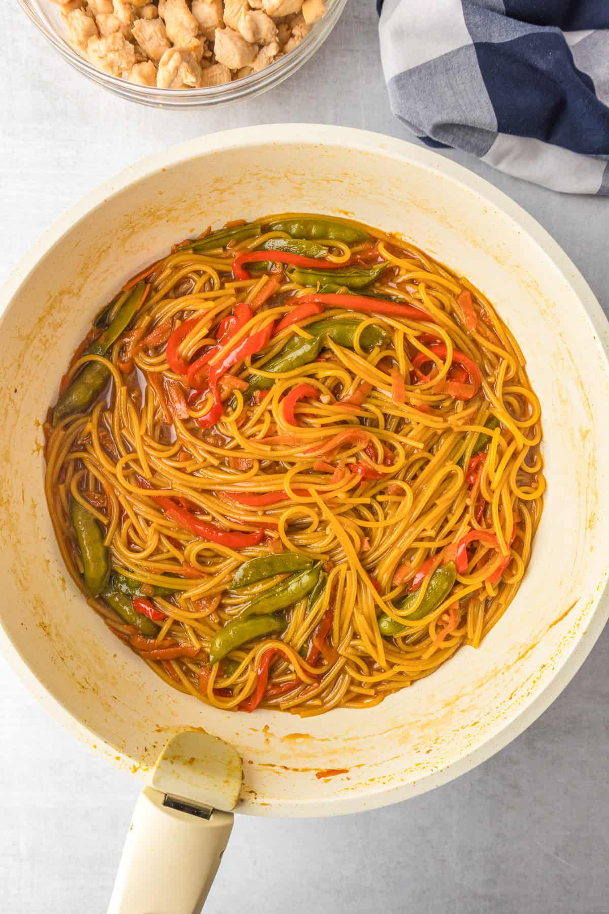 A pan filled with honey garlic chicken noodles, red bell peppers, and snap peas in a honey garlic sauce.