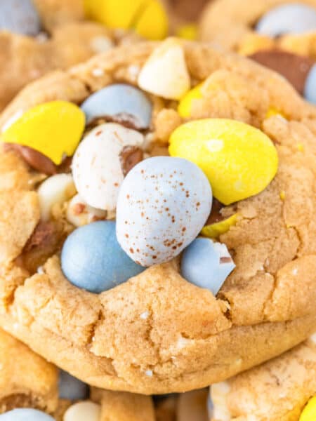 A close-up of mini egg chocolate chip cookies, topped with pastel-colored candy eggs and white chocolate chips.