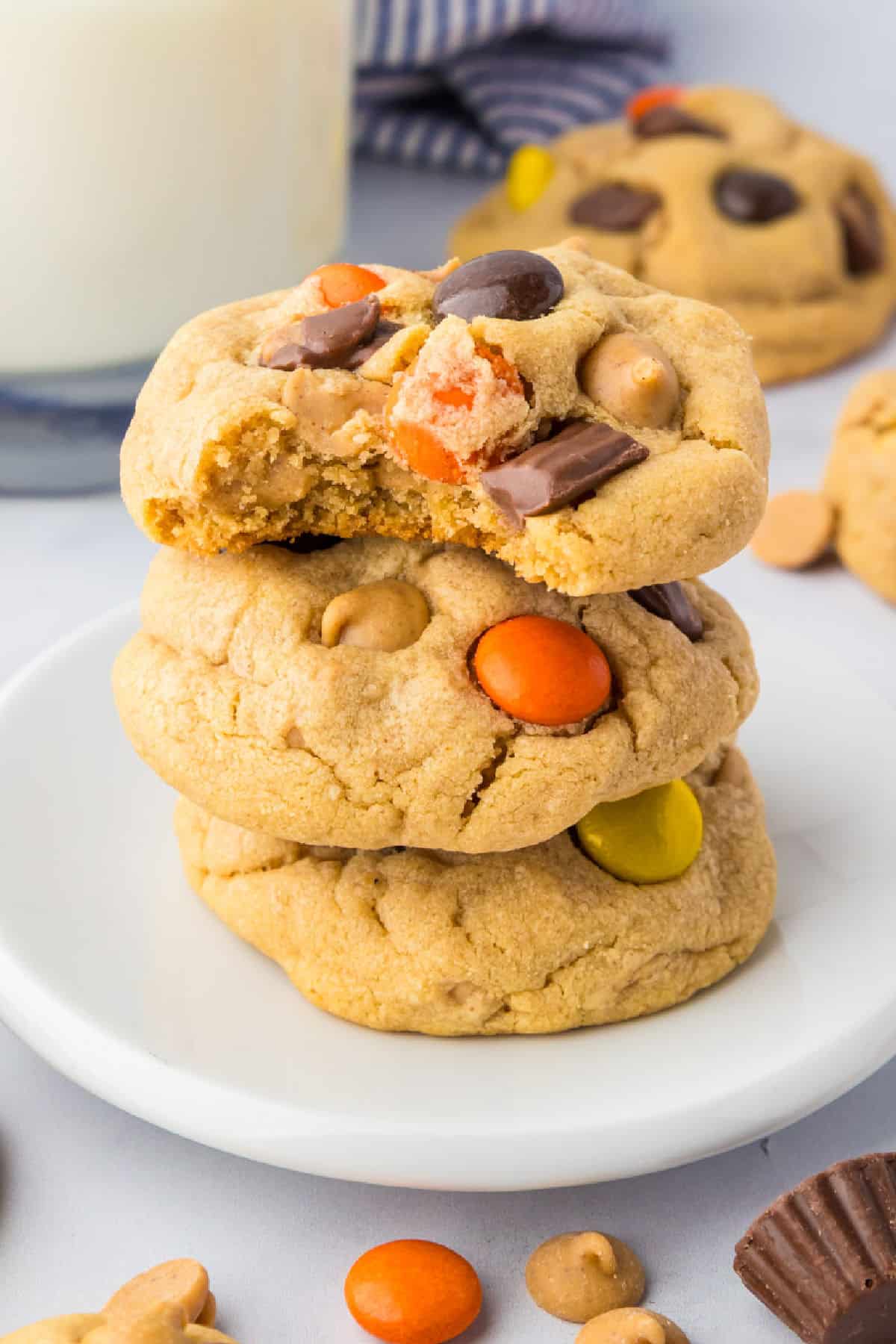 Three Reese’s Pieces peanut butter cookies stacked on a plate with the top cookie missing a bite.