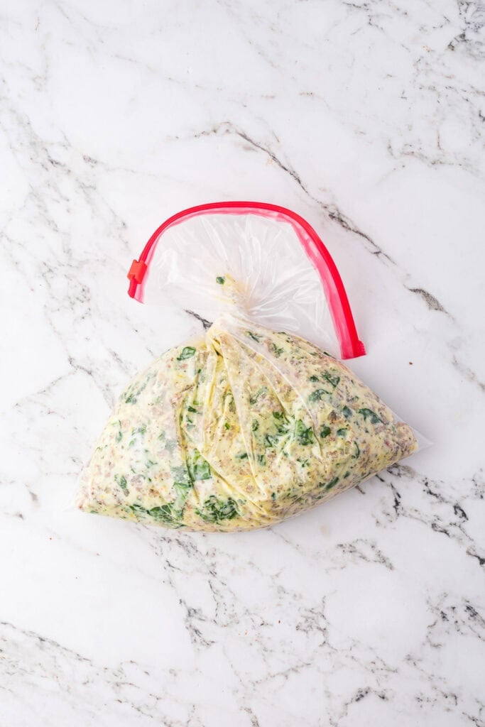A gallon size clear plastic zip-top bag filled with a mixture of sausage, cheese and spinach for the filling for manicotti with sausage and cheese.