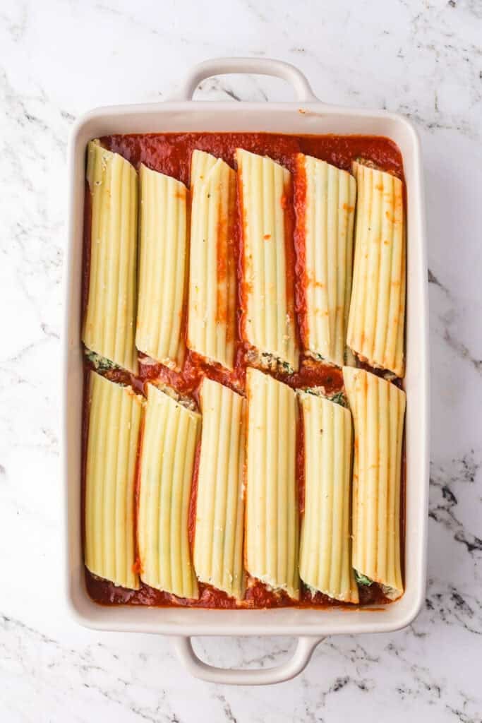 A white baking dish filled with cooked manicotti pasta stuffed with sausage and cheese, arranged over marinara.