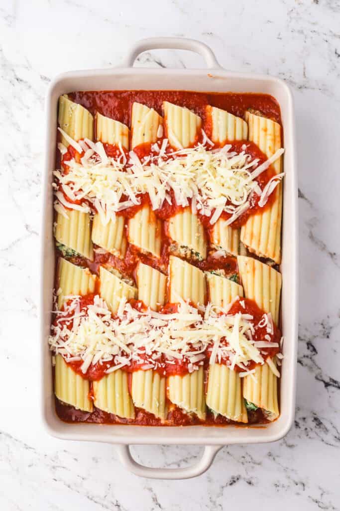 A baking dish filled with uncooked manicotti pasta stuffed with sausage and cheese and topped with sauce and cheese.
