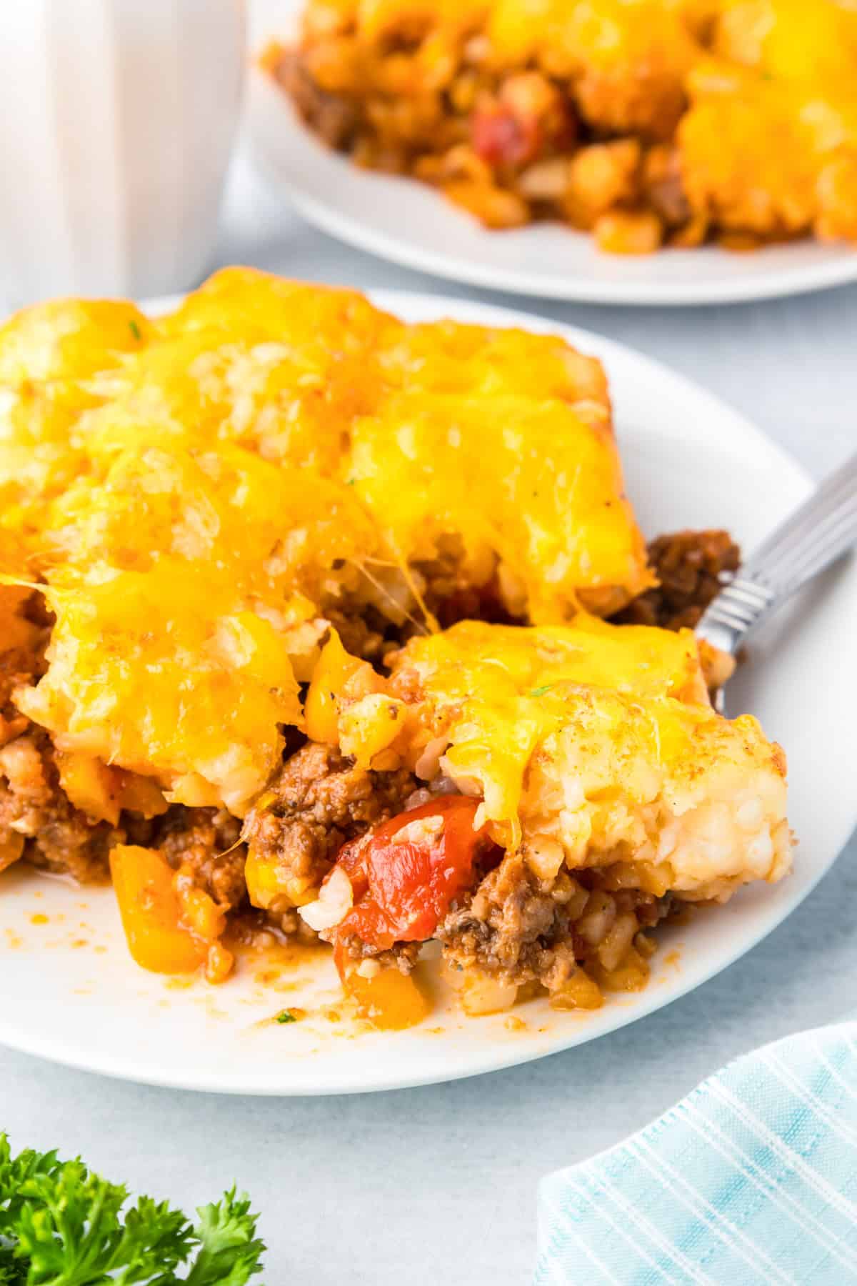 A serving of sloppy joe tater tot casserole on a plate with a fork scooping a bite.