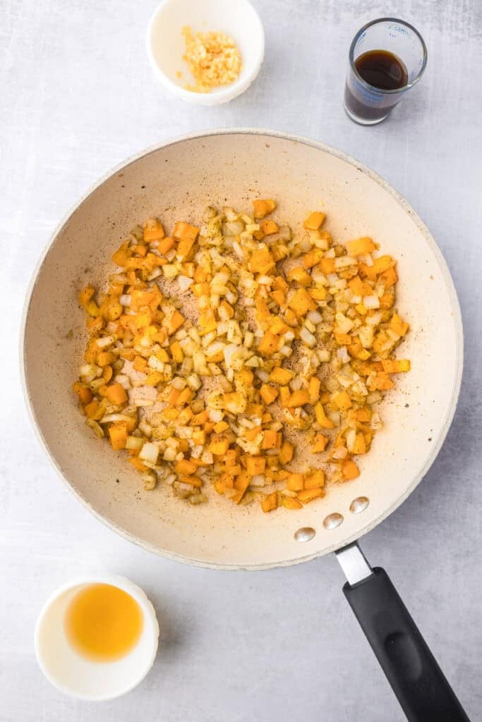 A skillet with saut&eacute;ed diced onions and orange bell peppers, surrounded by small bowls of chopped garlic, Worchestershire sauce, and apple cider vinegar for the meat filling for the sloppy joe tater tot casserole.