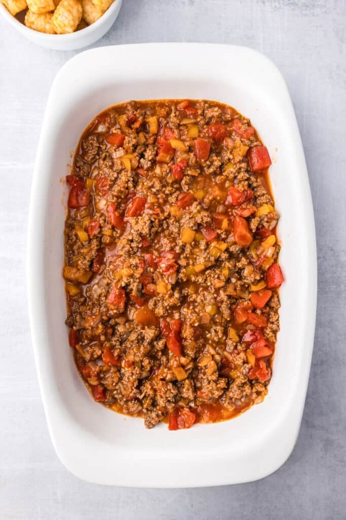 A white casserole dish filled with sloppy joe tater tot casserole meat filling.