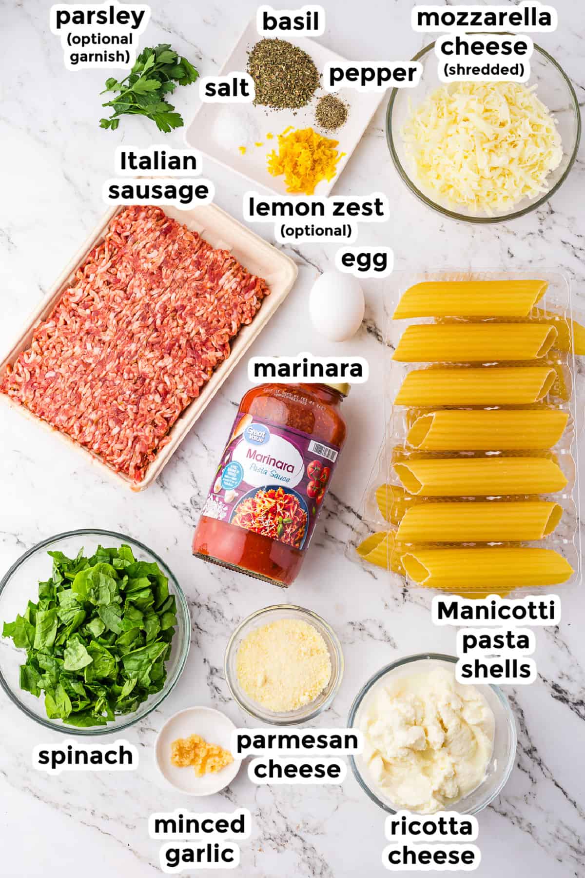 Ingredients for manicotti with sausage and cheese laid out on a white surface with text labels.